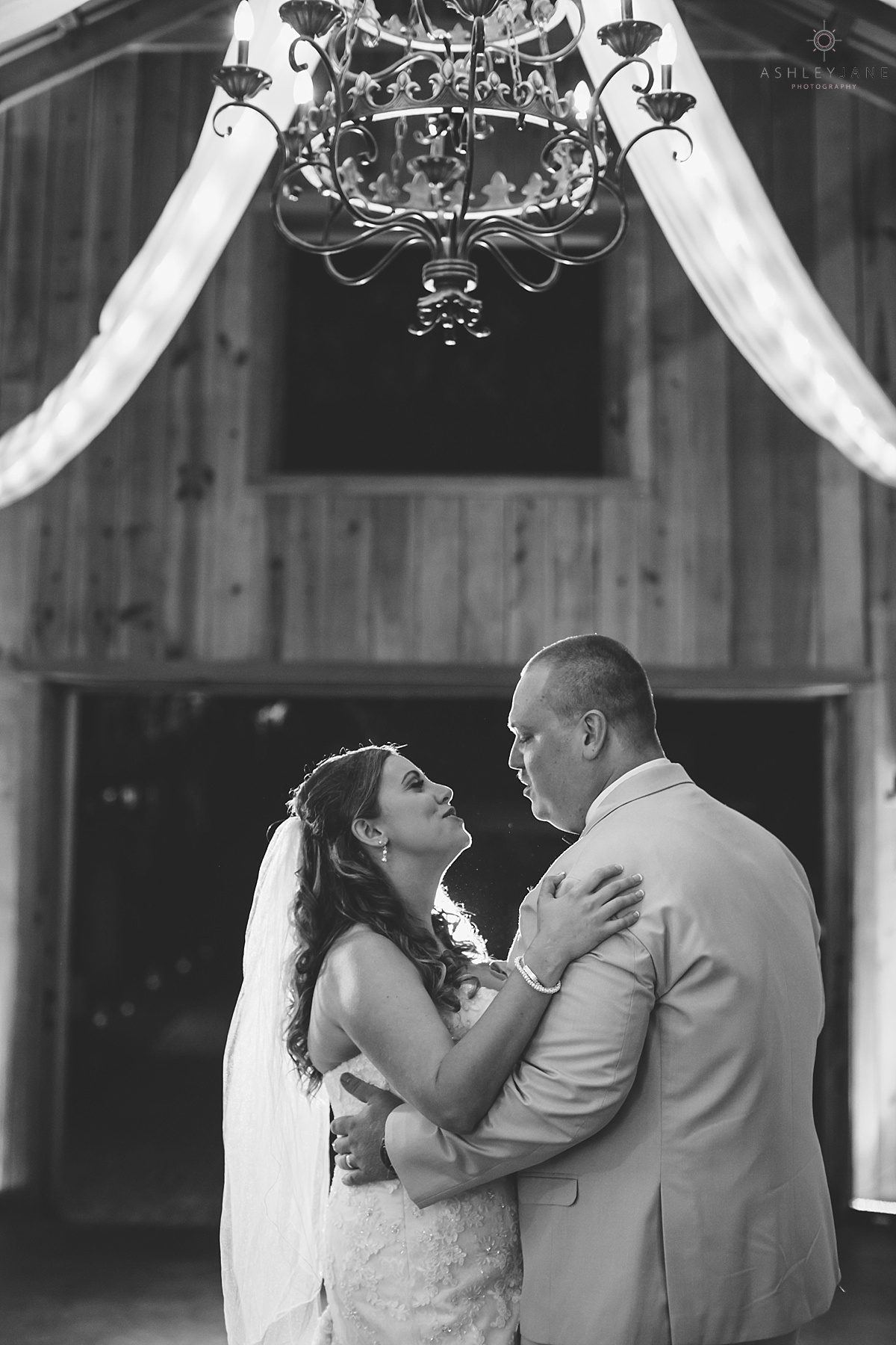 bride and groom in rustic wedding reception under chandelier singing to one another during first dance