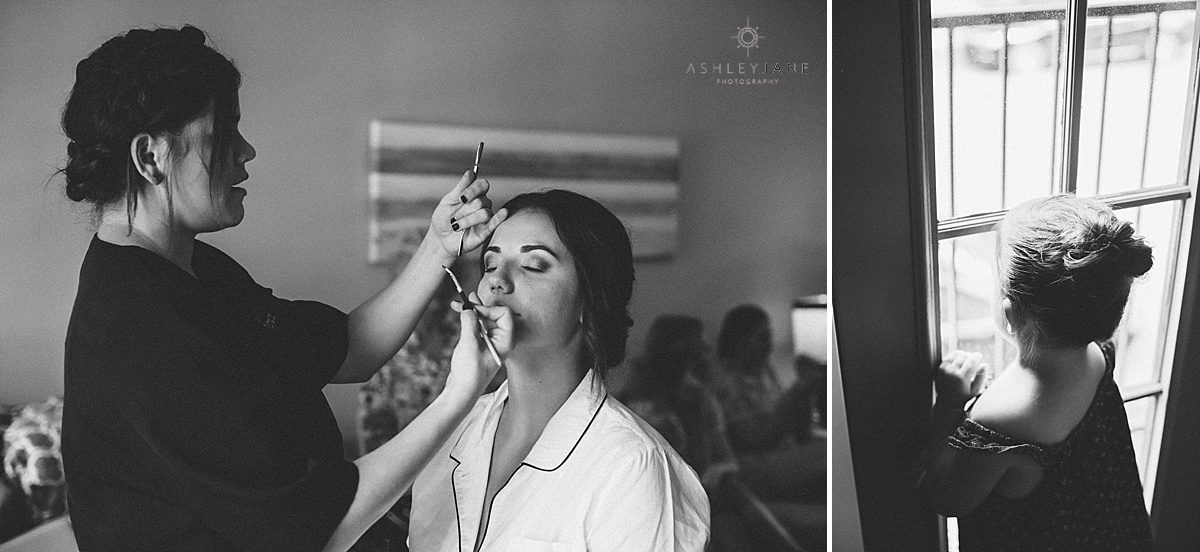 Bride getting her makeup done on her wedding day while flower girl looks out the window