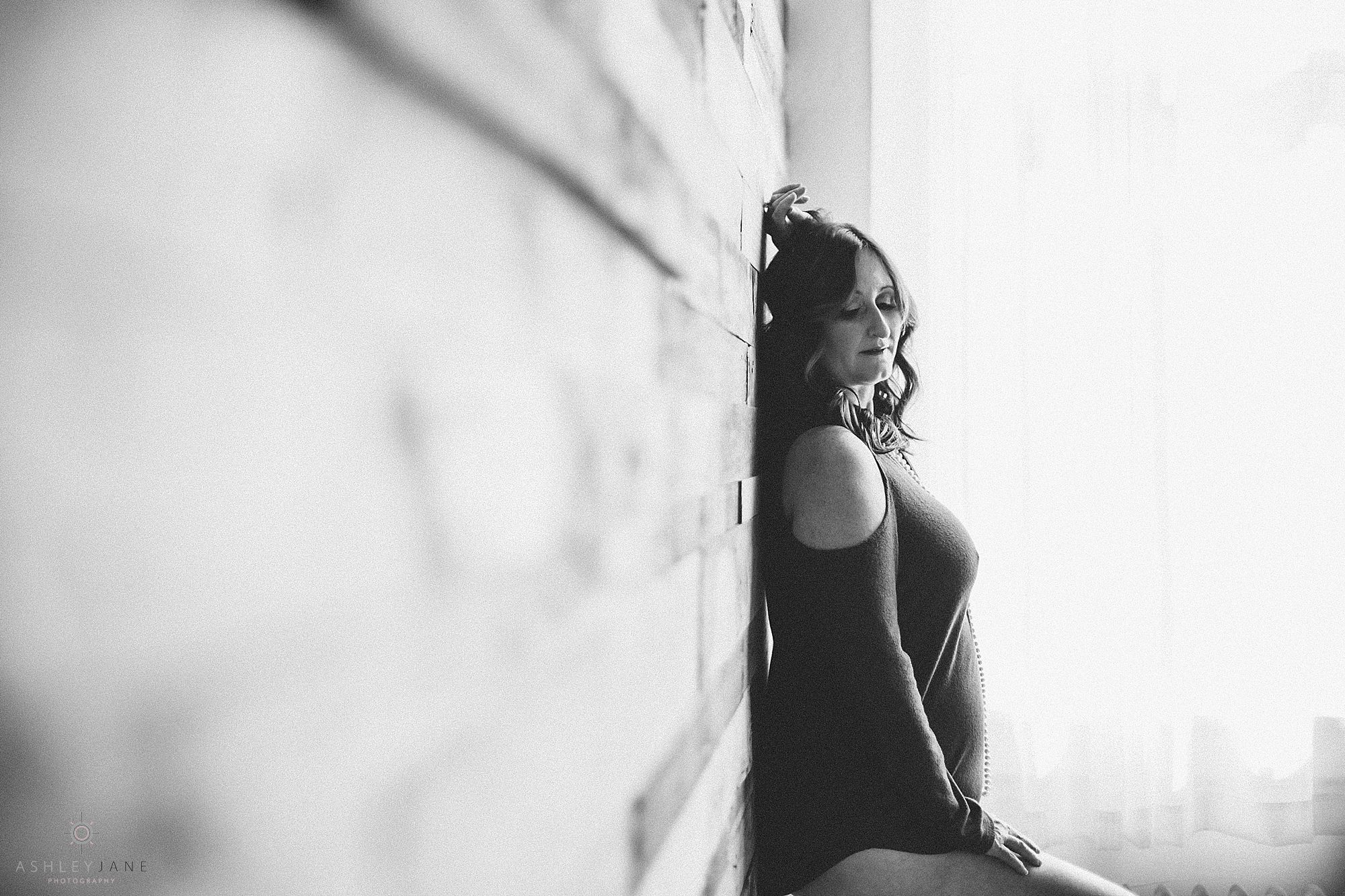 Boudoir black and white image of woman up against wood wall with cold shoulder shirt on and she is looking down. Shot by Orlando boudoir photographer.