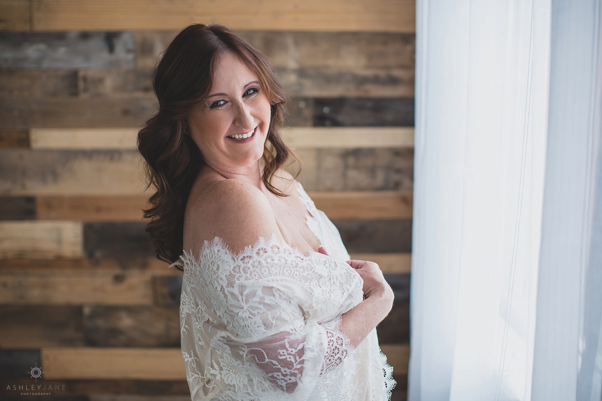 Woman standing with lace robe over her shoulders with a super big happy smile on her face, shot by boudoir photographer in Orlando.
