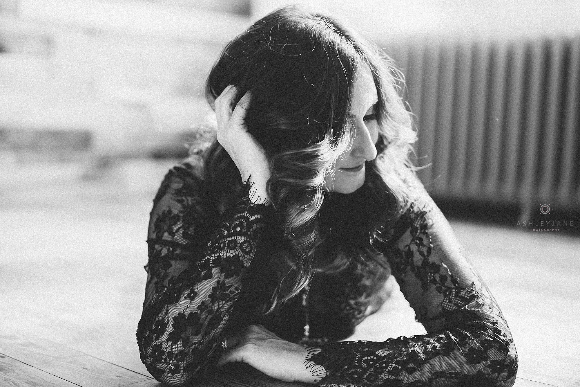 Black and white image of woman laying on floor on her chest in black lace dress with hand in her hair shot by Orlando boudoir photographer
